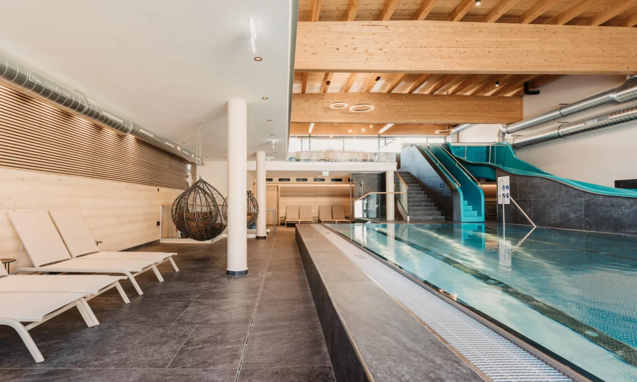 Modern gestalteter Family Pool im Hofgut Wagrain mit Wasserrutsche, gemütlichen Relaxliegen und Schwebesesseln – der perfekte Ort für Familienauszeit und Spielspaß im Wasser.