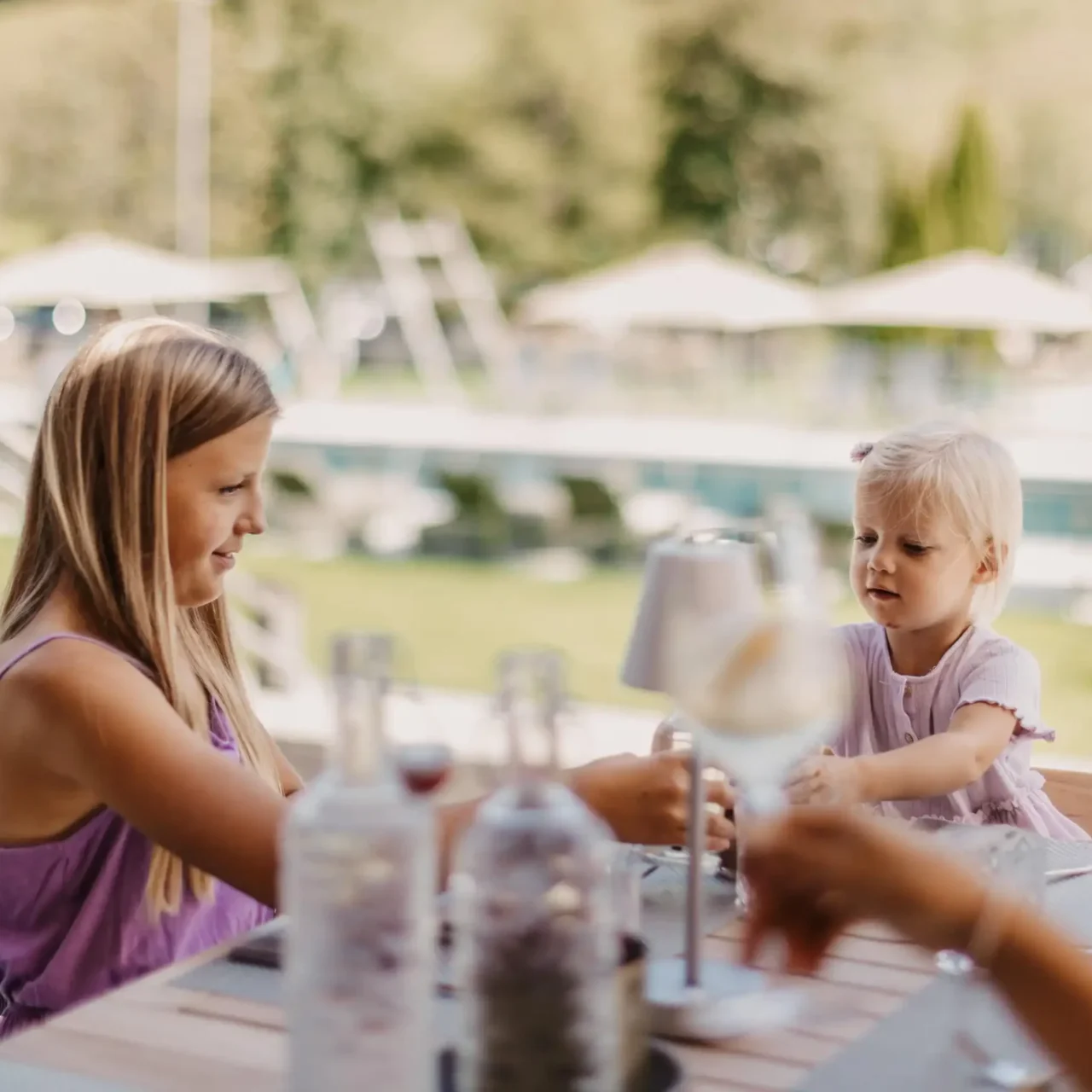 Gemeinsame Familienzeit auf der Sonnenterrasse des Hofgut Wagrain – fröhliche Kinder, liebevolle Momente und entspanntes Beisammensein mit Blick auf Pool und Natur. Hier wird der Sommer zum Familienerlebnis.