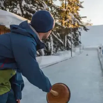 Tradition meets winter fun - curling amidst a snow-covered mountain landscape at sunset.