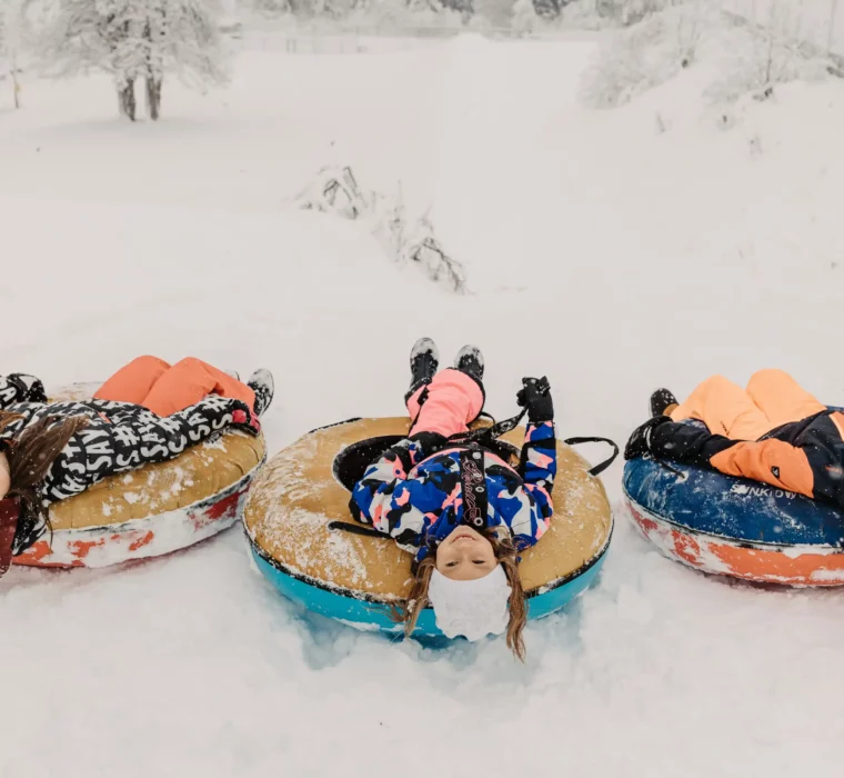 Tre børn griner på snowtubes i sneen - ren vinterglæde og kælkesjov på Hofgut Wagrain.