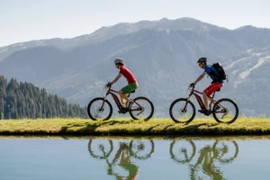 Two sporty guests enjoy a panoramic e-bike tour along a crystal-clear mountain lake in Wagrain - active time out with the enjoyment of nature and a feeling of alpine freedom.