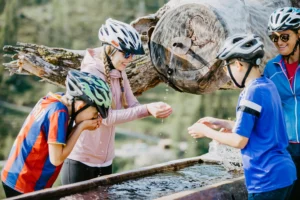 Family refreshing themselves at a rustic mountain spring during their cycle tour - crystal-clear spring water, smiling faces and an unforgettable moment in the Salzburg countryside.