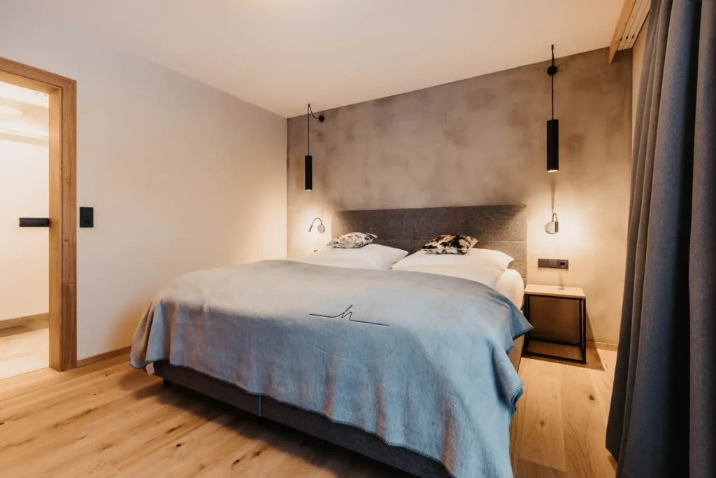 Cosy bedroom with modern box-spring bed, minimalist lighting, wooden flooring and soft natural tones - stylish design with alpine flair.