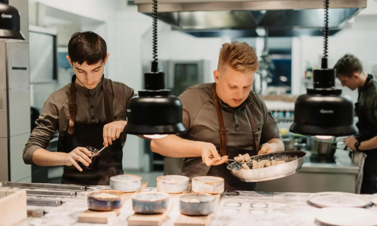 Koks bij het bereiden en serveren van gerechten in een open, modern uitgeruste hotelkeuken – focus op teamwork en culinaire precisie.