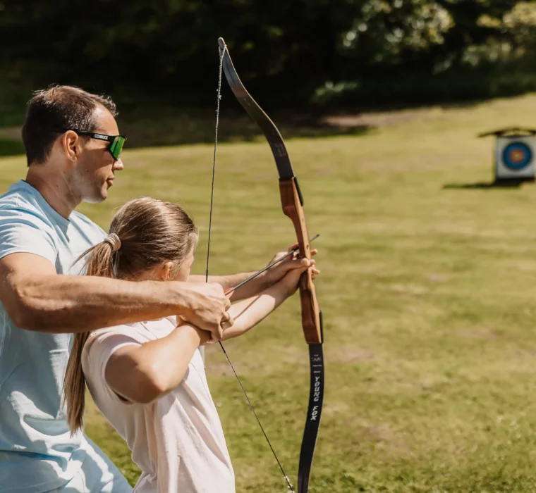 Mikken op het doel op vakantie - gezamenlijk boogschieten voor kinderen en volwassenen op de weide in de zon.