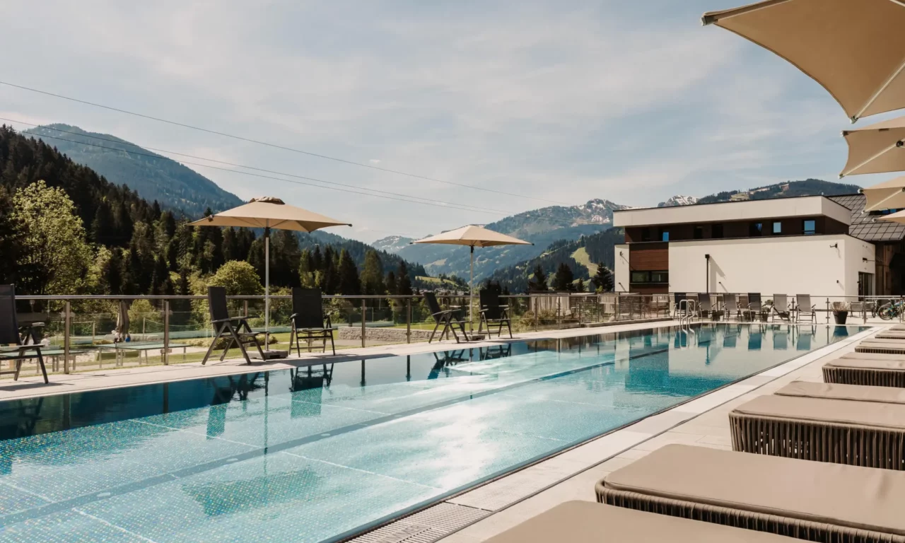 25-Meter-Sportbecken im Hofgut Wagrain mit Sonnenliegen und Schirmen – Sommerliche Ruheoase mit Bergblick für aktive und entspannte Urlaubstage im Salzburger Land.