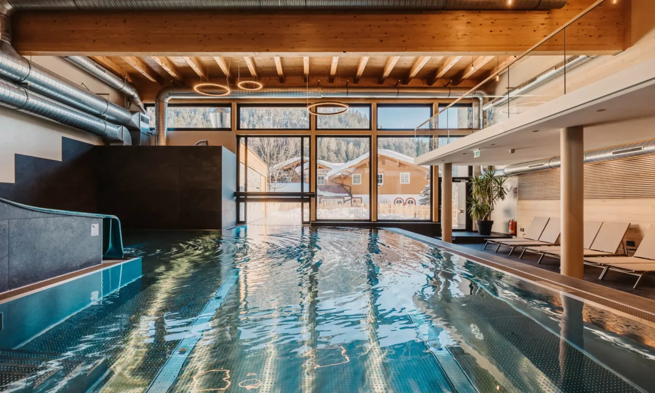 Hofgut-aparment-lifestyle-resort-wagrain Indoor-outdoorpool-128 Sfeervolle opname van het overdekte zwembad van Hofgut Wagrain met uitzicht op de besneeuwde vallei - gezellige warmte, modern design en een unieke plek om even stil te staan.