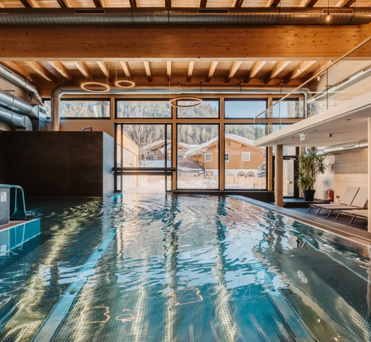 Atmospheric shot of the indoor pool at Hofgut Wagrain with a view of the snow-covered valley - cosy warmth, modern design and a unique place to pause for a moment.