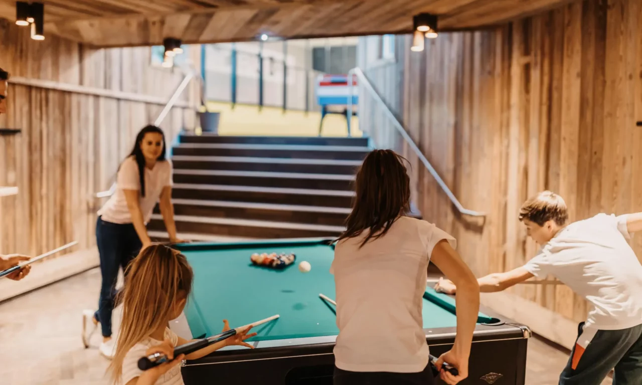 Kinder und Jugendliche spielen gemeinsam Billard in einem gemütlichen Freizeitraum mit Holzverkleidung – aktive Indoor-Zeit für die ganze Familie im Urlaubsresort.