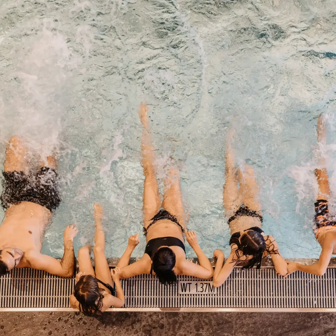 Familie und Kinder planschen gemeinsam am Beckenrand eines beheizten Pools, spritzen Wasser und genießen ausgelassenen Badespaß – perfekte Urlaubsmomente im Familienresort.