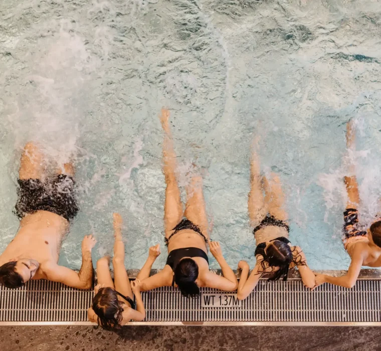 Family and children splash around together at the edge of a heated pool, splash water and enjoy exuberant bathing fun - perfect holiday moments at the family resort.