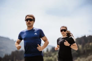 Running enjoyment in the midst of nature - sporty couple trail running through the blooming meadows and forests around Hofgut Wagrain in Salzburger Land.