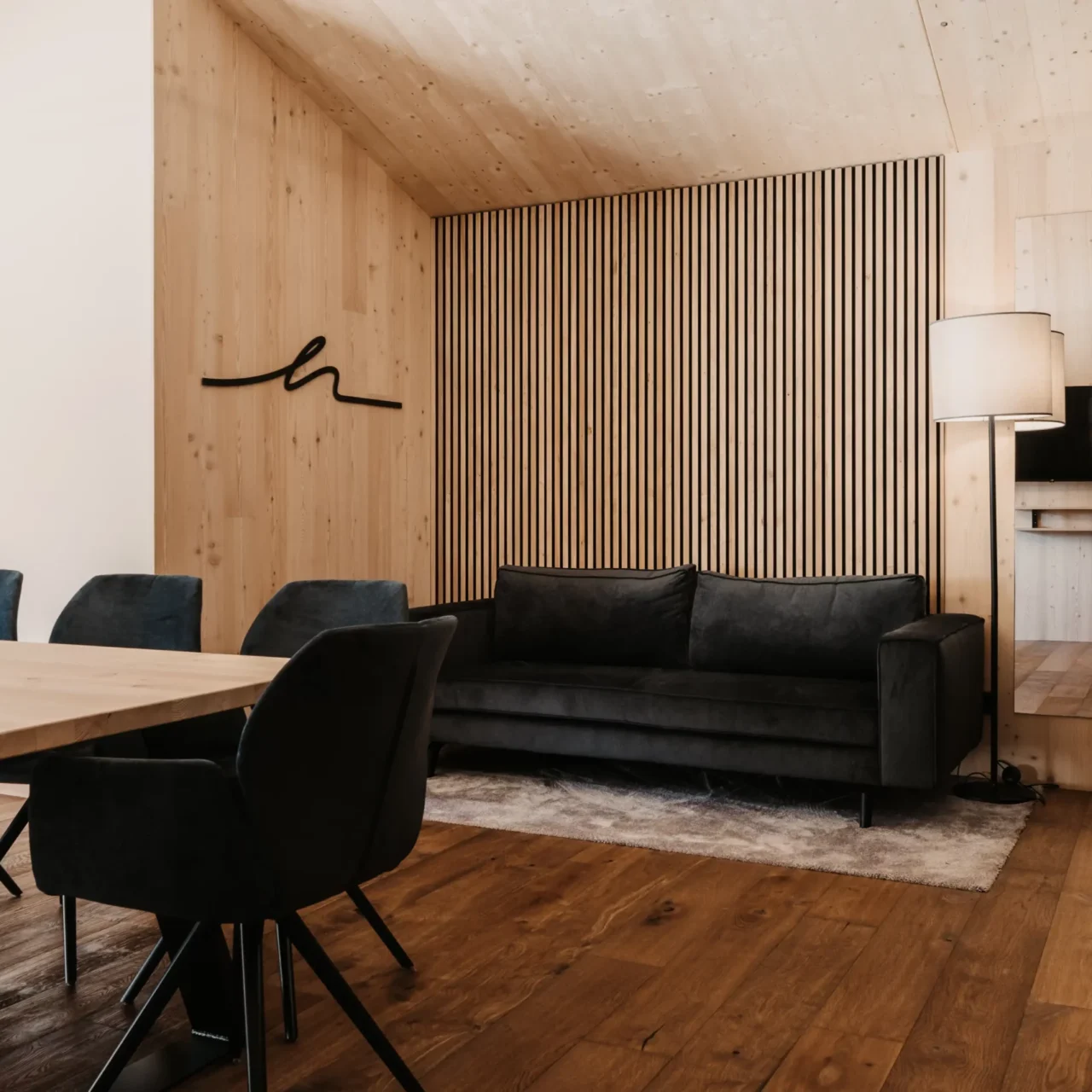 Gemütlicher Wohnbereich im Hofgut Wagrain: Edles Sofa vor stilvoller Holzvertäfelung, warme Lichtakzente und modernes Interior für entspannte Familienmomente im alpinen Ambiente.