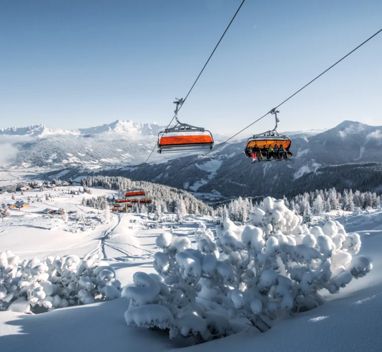Skilift mit orangenen Wetterschutzhauben im verschneiten Skigebiet Flachau mit Blick auf die Alpen.