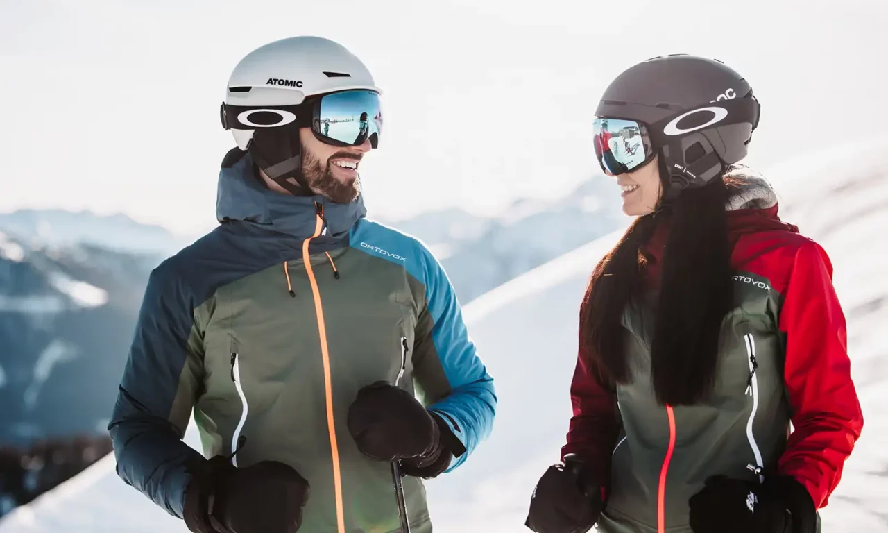 Skifahrerpaar im Skiurlaub in Österreich mit Helmen und Ortovox-Jacken in den Alpen.