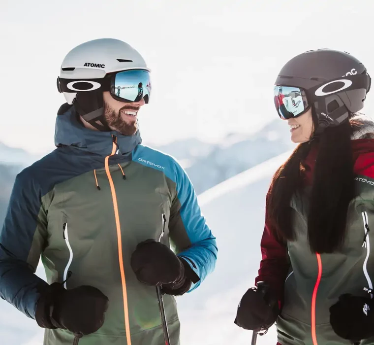 Skiing couple on a skiing holiday in Austria with helmets and Ortovox jackets in the Alps.