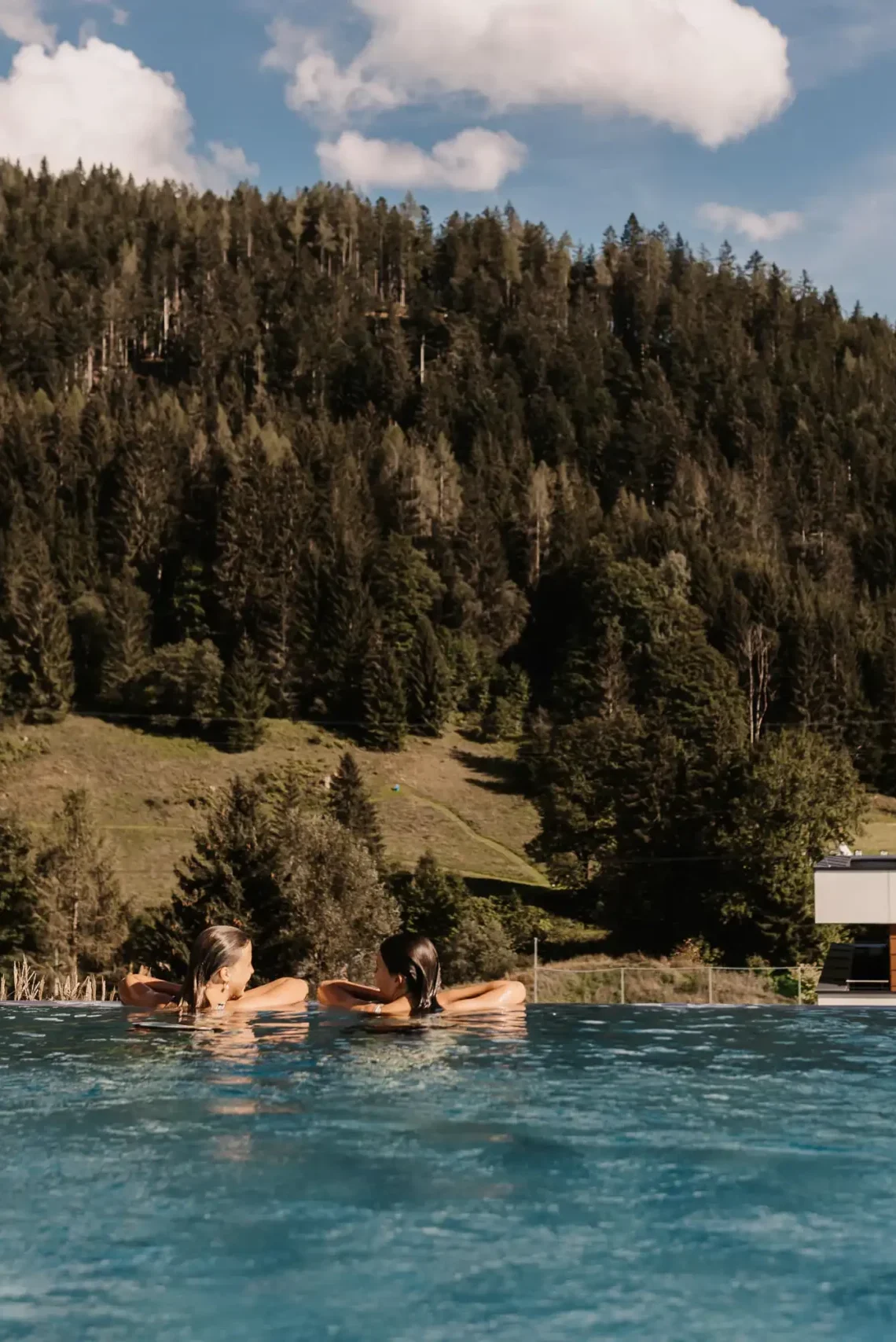 Zwei Gäste genießen den Moment im Infinity-Pool des Hofgut Wagrain – mit atemberaubendem Blick auf die umliegenden Berge und Wälder. Pure Entspannung und alpines Lebensgefühl vereint an einem ganz besonderen Ort.