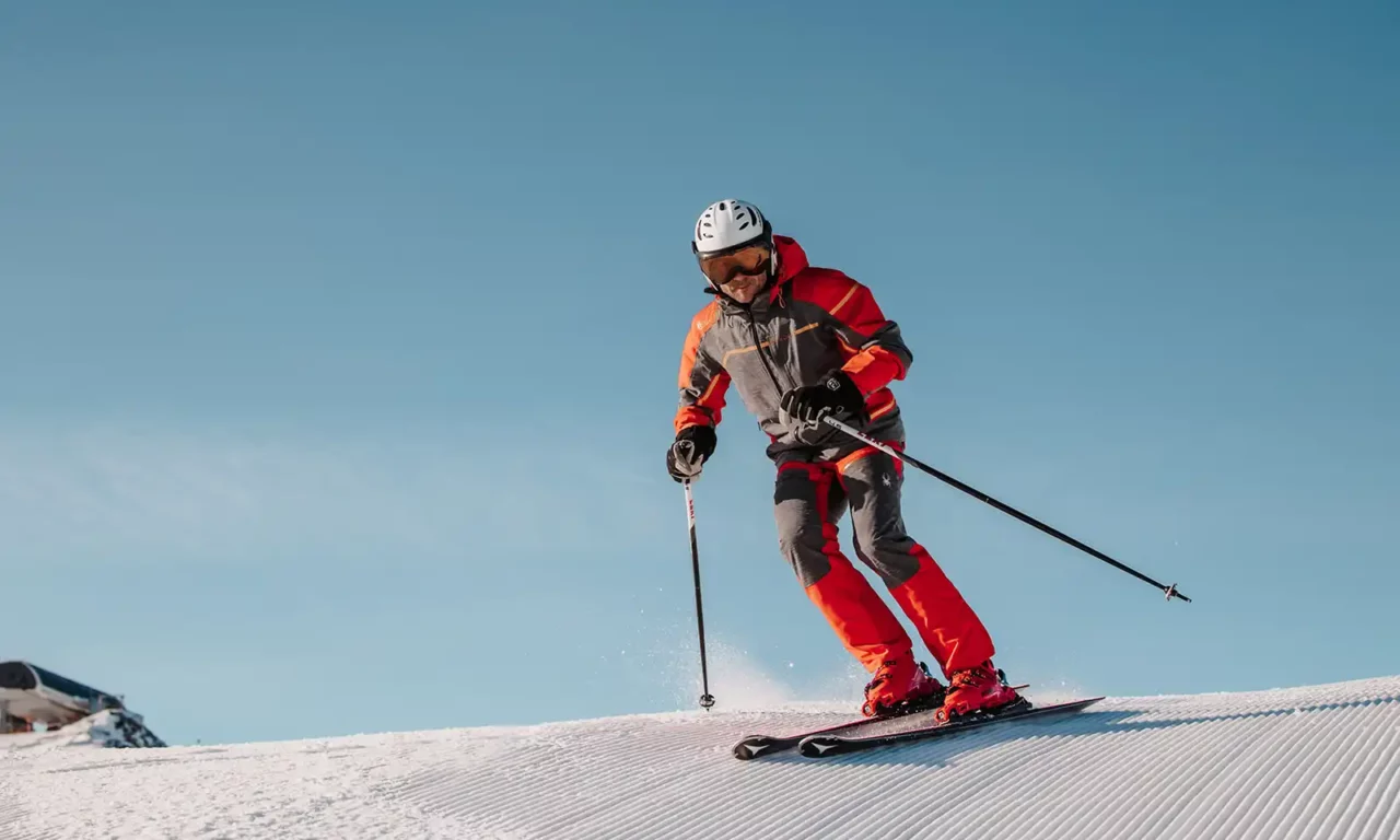 Hofgut_Winter©Elisabeth_Fotografie-57-Ski-Model-roter-Skianzug Skiër in een rood skipak maakt bochten op perfect geprepareerde pistes in Ski Amadè.