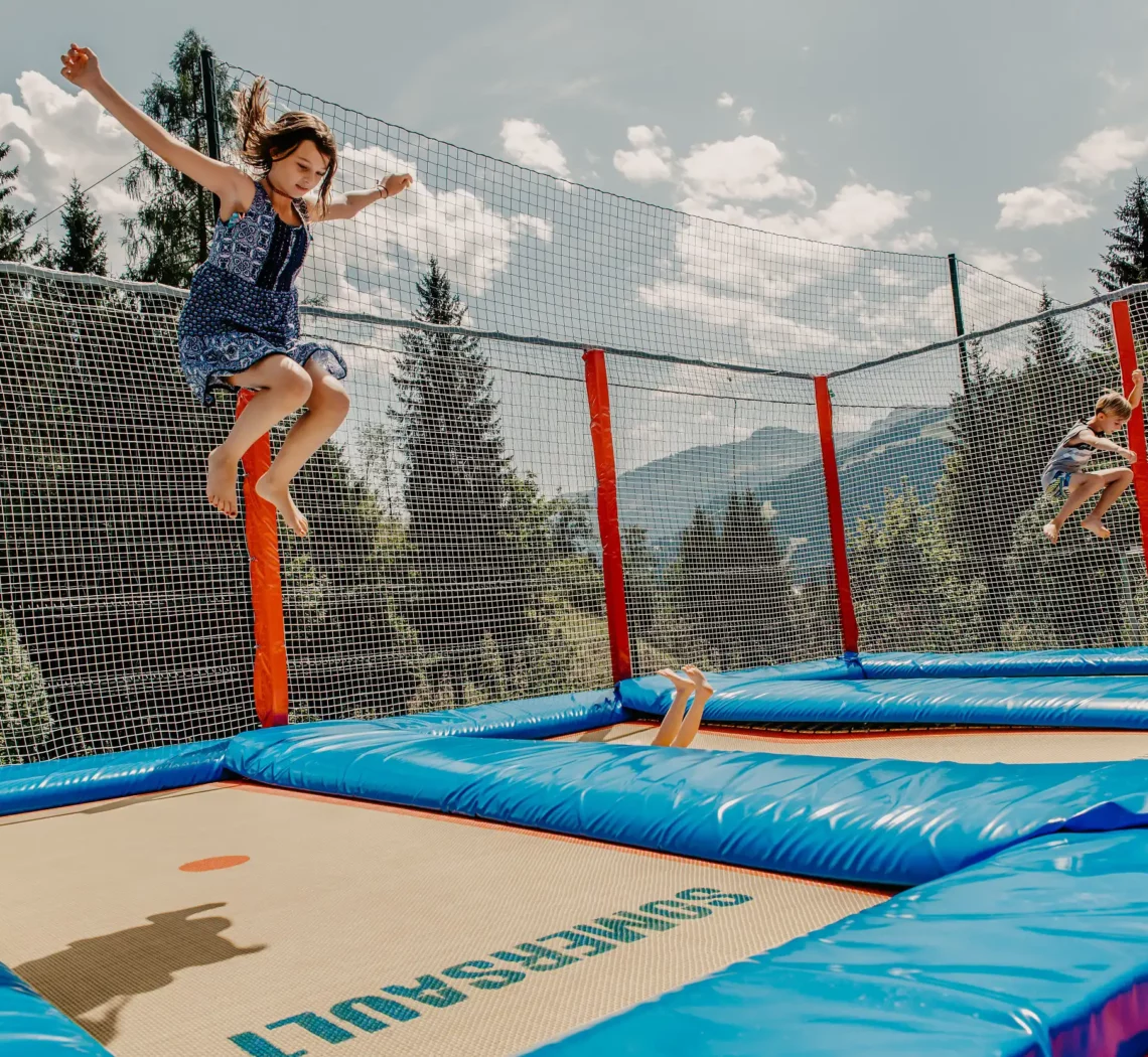 Hofgut-Apartment-lifestyle-resort-erleben-fuer-Kinder-Outdoor-Trampolinanlage Kinder springen auf dem Trampolin im Hofgut Wagrain vor alpiner Kulisse im Sommerurlaub