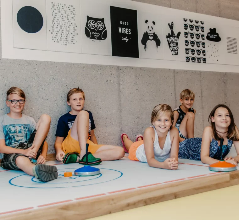 Hofgut-Wagrain-Apartment-Lifestyle-Resort-Erleben-im-Hofgut-für-Kinder-Stockbahn Kinder beim Stockschießen in der Indoor-Games Area im Hofgut Wagrain.