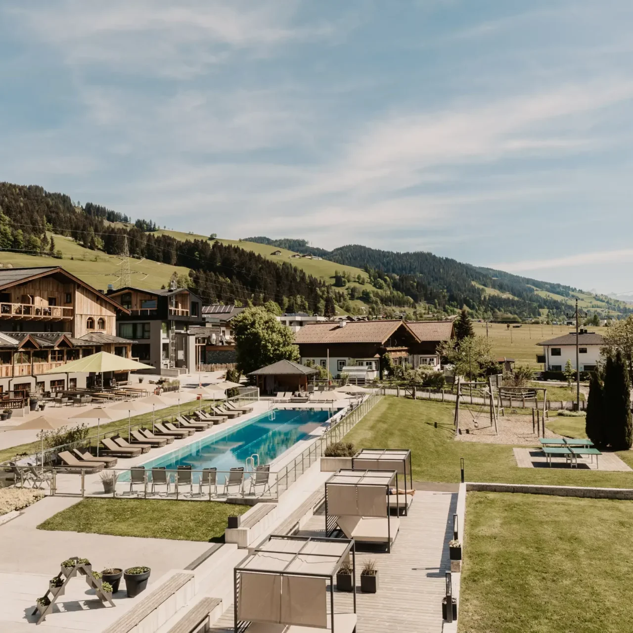 Slunečný letní výhled na venkovní bazén a zahradu Hofgut Wagrain s panoramatickým výhledem na Alpy