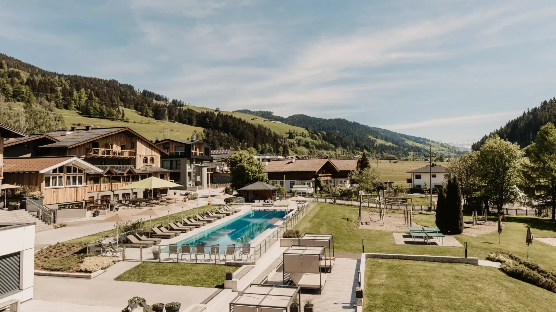 Sommeridylle im Hofgut Wagrain - alpines Lebensgefühl trifft auf Entspannung im 25-Meter-Sportbecken, umgeben von Sonnenliegen, Liegestühlen und grüner Bergkulisse.