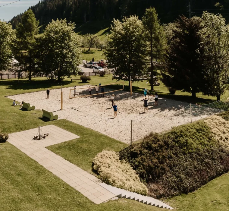Hofgut-Wagrain-Apartment-Lifestyle-Resort-Wagrain-erlebenoutdoor-beachvolleyball 404 Gäste spielen Beachvolleyball im Hofgut Wagrain umgeben von Bäumen und Bergpanorama