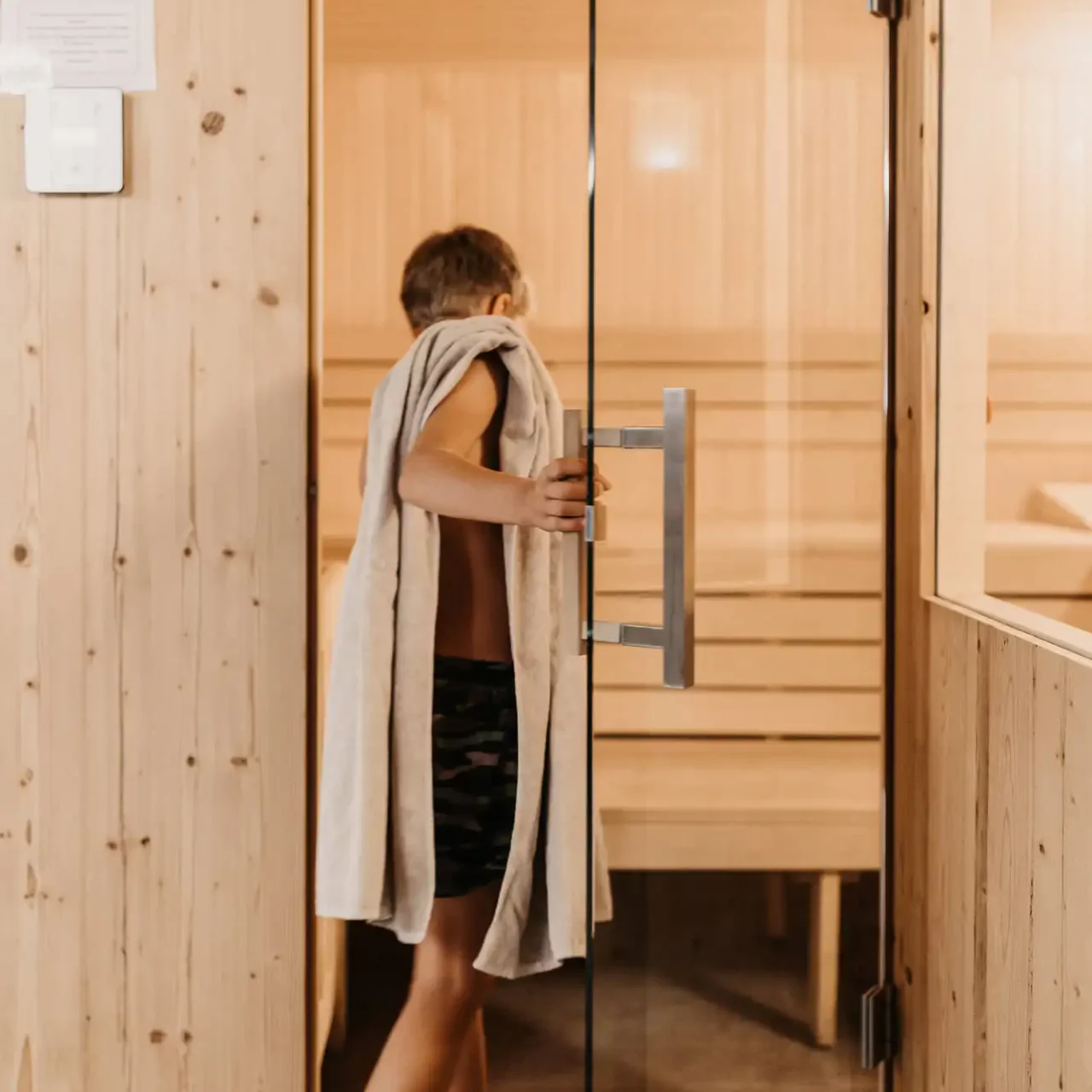 Hofgut-Wagrain-Apartment-Resort-Wagrain 434 A boy stands with a towel in front of the family-friendly textile sauna at Hofgut Wagrain - relaxing wellness moments for young guests too.