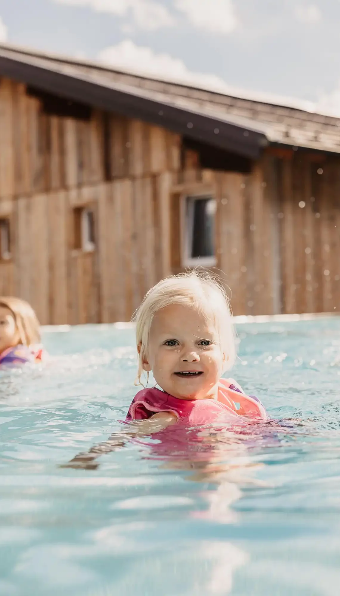 Kleines Kind mit Schwimmhilfe im Outdoorpool des Hofgut Wagrain beim Baden mit der Familie