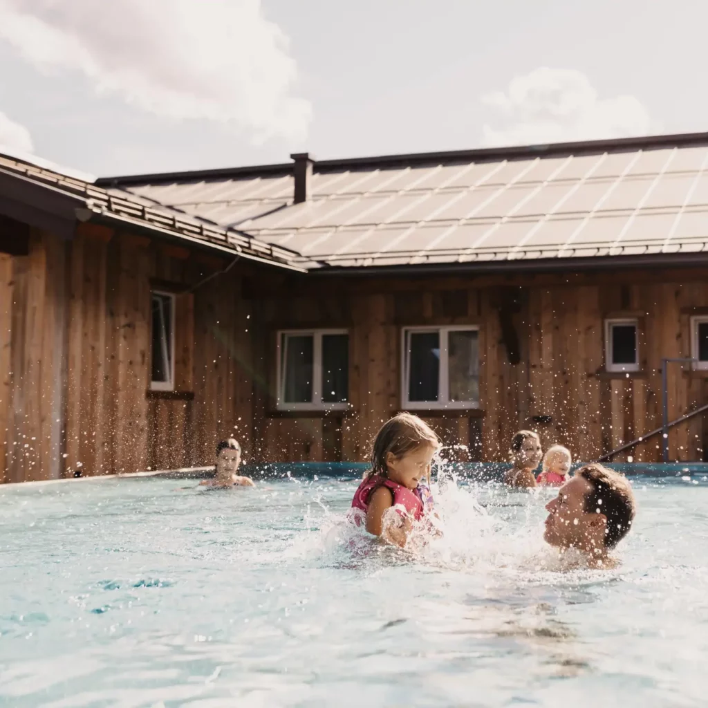 Hofgut-Wagrain-Apartment-Resort-Wagrain 605 Carefree family time in the infinity pool at Hofgut Wagrain - a father laughingly lifts his daughter into the air while the sun's rays and the alpine backdrop create real holiday magic.