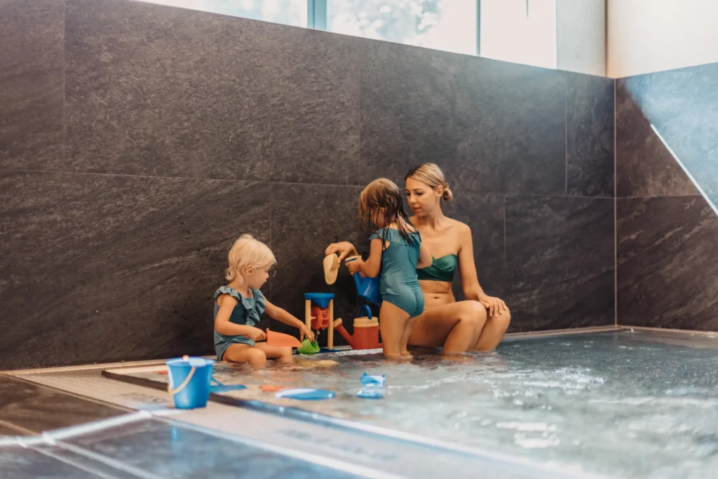 Gemeinsame Spielzeit im Babypool – eine Mutter genießt mit ihren beiden kleinen Töchtern die entspannte Atmosphäre im warmen Wasserbereich des Hofgut Wagrain, umgeben von liebevollen Details und kindgerechten Wasserspielsachen.