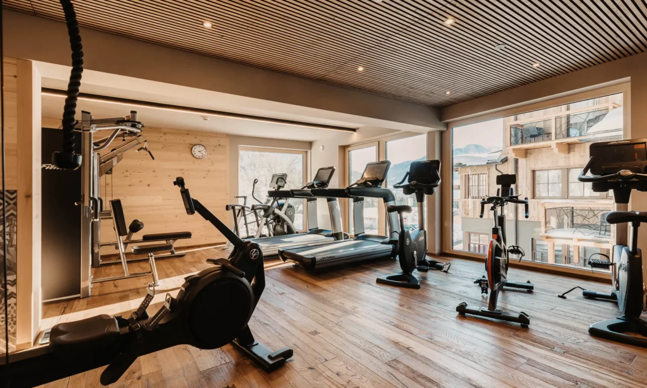 Hofgut-aparment-lifestyle-resort-wagrain-fitnessstudio-115 Modernes Fitnessstudio im Hofgut Wagrain mit hochwertigen Geräten, Holzdesign und Blick auf die verschneiten Berge.