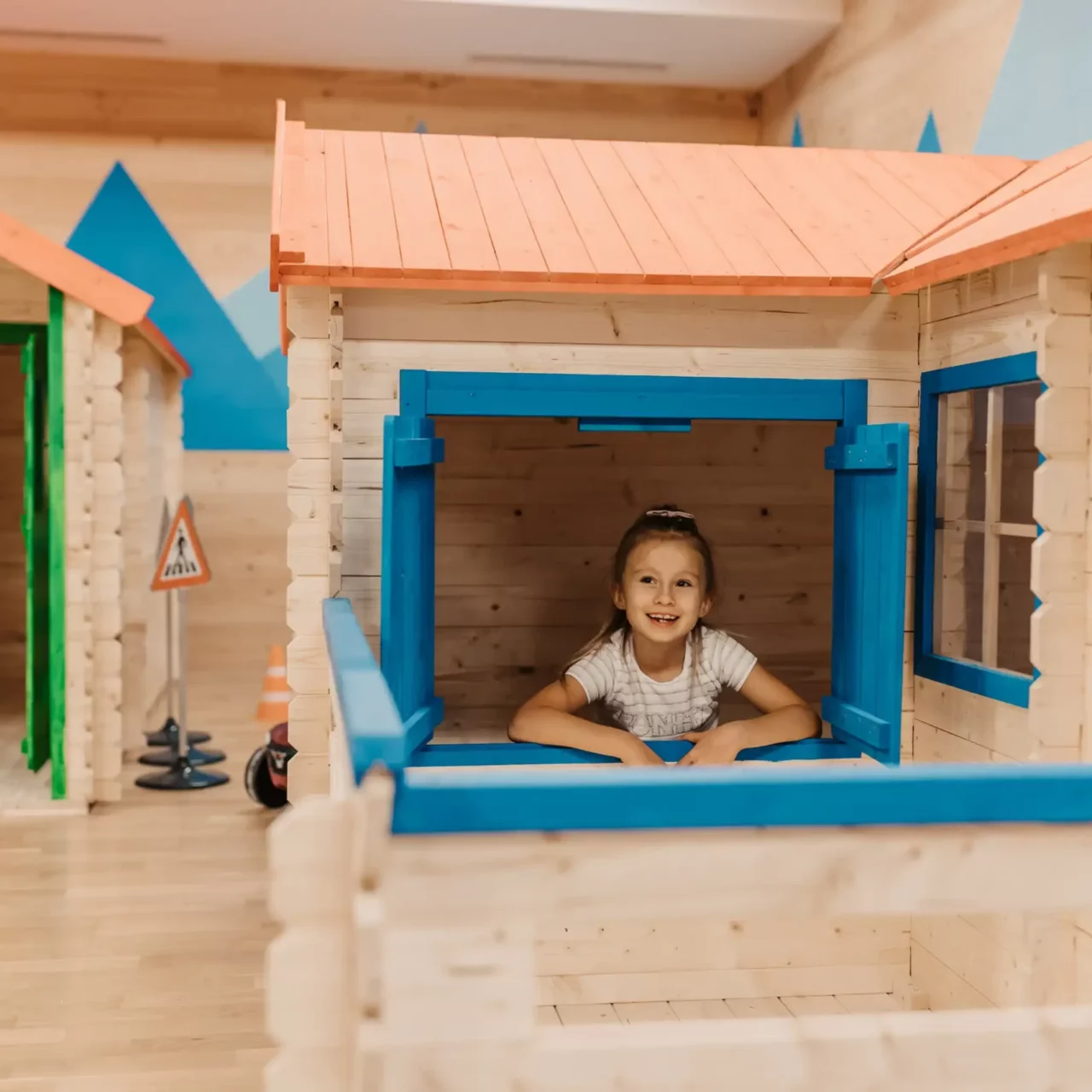 Spielerisches Entdecken im Mini Park: Ein fröhliches Mädchen blickt aus dem Fenster eines liebevoll gestalteten Spielhäuschens im Hofgut Wagrain – ein Ort voller Fantasie, Abenteuer und kindlicher Freude.