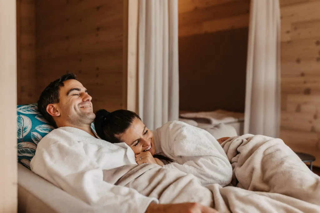 Hofgut-wagrain-apartment-adults-only-Elternzeit-259 Zweisamkeit genießen im Hofgut Wagrain – ein entspanntes Paar kuschelt eingehüllt in flauschige Bademäntel auf einer gemütlichen Liege im Ruheraum. Warme Holzoptik und Geborgenheit machen diesen Moment unvergesslich.