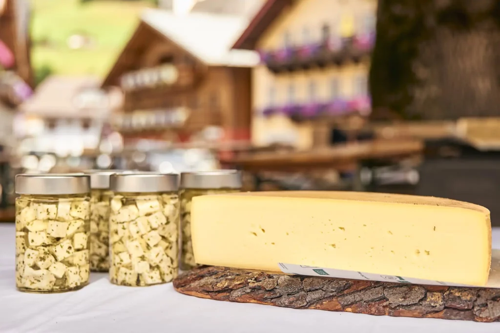 Hofgut-wagrain-apartment-lifestyle-resort-shop-Molkereiprodukte-Bio-aus-dem-Tal Regional cheese delicacies from Salzburger Land: fresh semi-hard cheese and flavoursome herbed sheep's cheese in a jar - presented against a traditional Alpine backdrop.