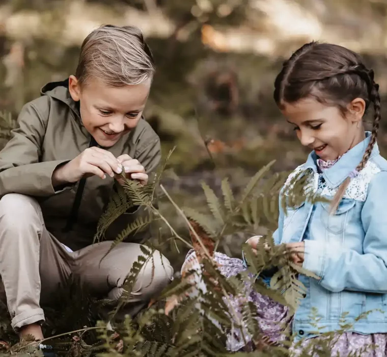 Un bambino e una bambina giocano felici tra le felci della foresta.