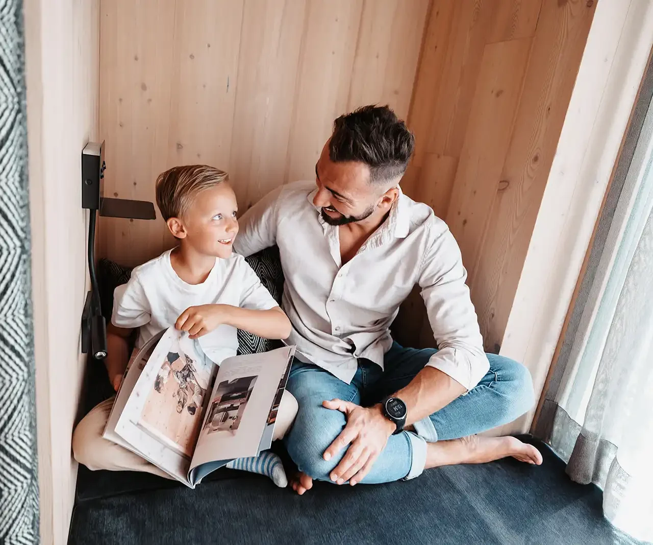 Vater und Sohn sitzen gemütlich in einer holzverkleideten Nische und blättern zusammen in einem Magazin.