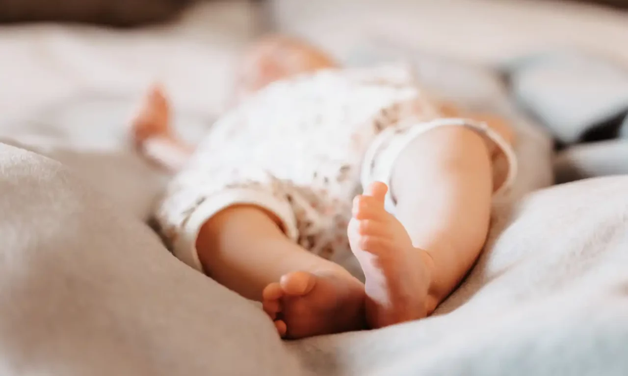 Close-up of the bare feet of a sleeping child on a soft grey blanket.