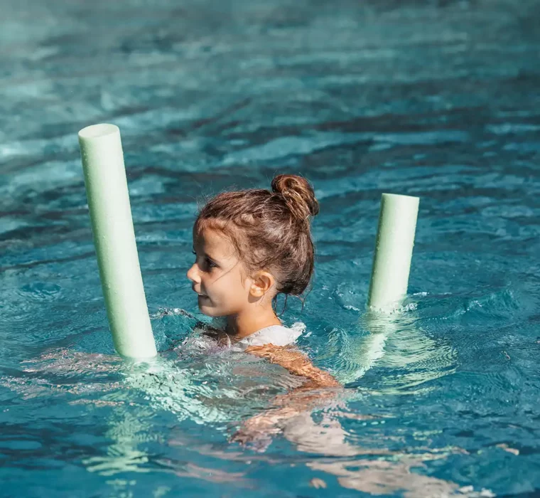 Hofgut©Elisabeth_Fotografie-538 Ein Mädchen spielt lachend mit einer Poolnudel im Wasser.