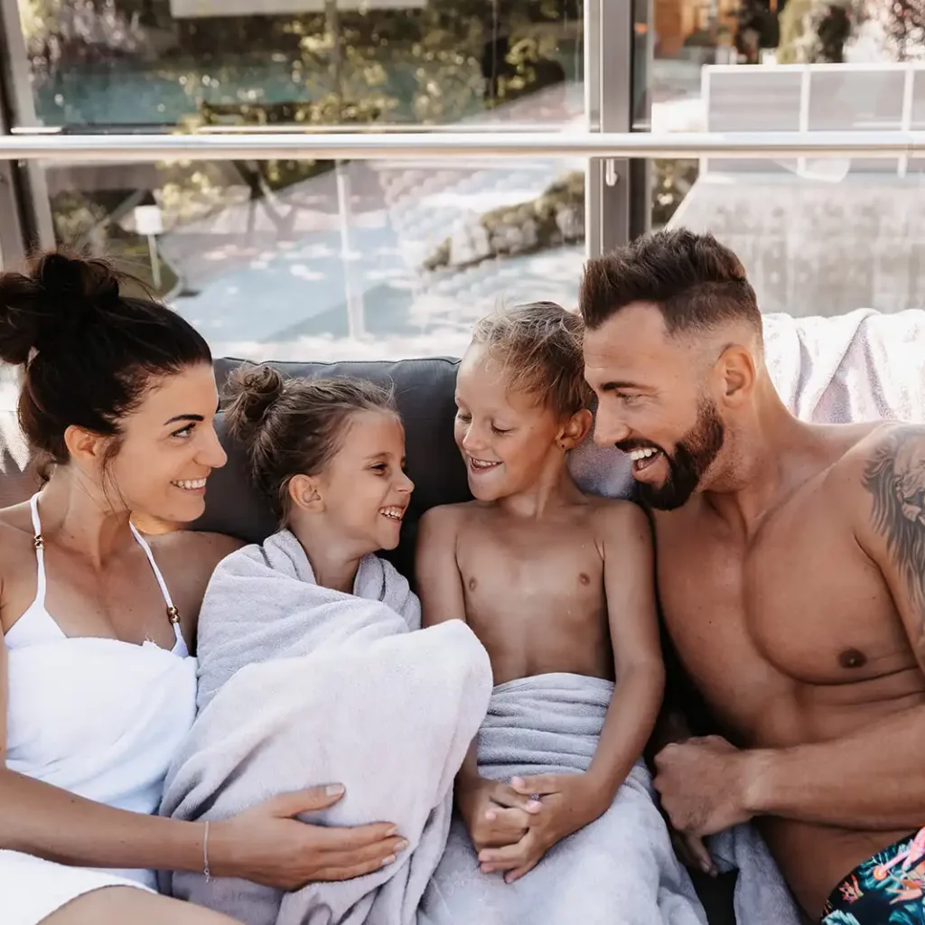 Hofgut©Elisabeth_Fotografie-575 Family relaxing together on a large outdoor lounger, wrapped in towels, after a swim.