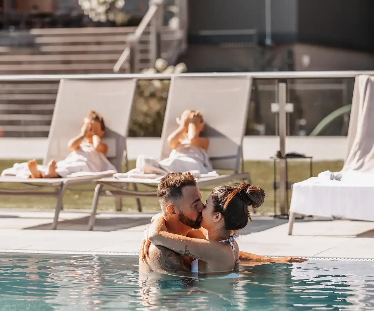 Romantic moment on a family holiday - a couple enjoying intimate togetherness in the pool at Hofgut Wagrain while the children relax on the sun loungers. Holiday bliss for young and old in the midst of an Alpine idyll.