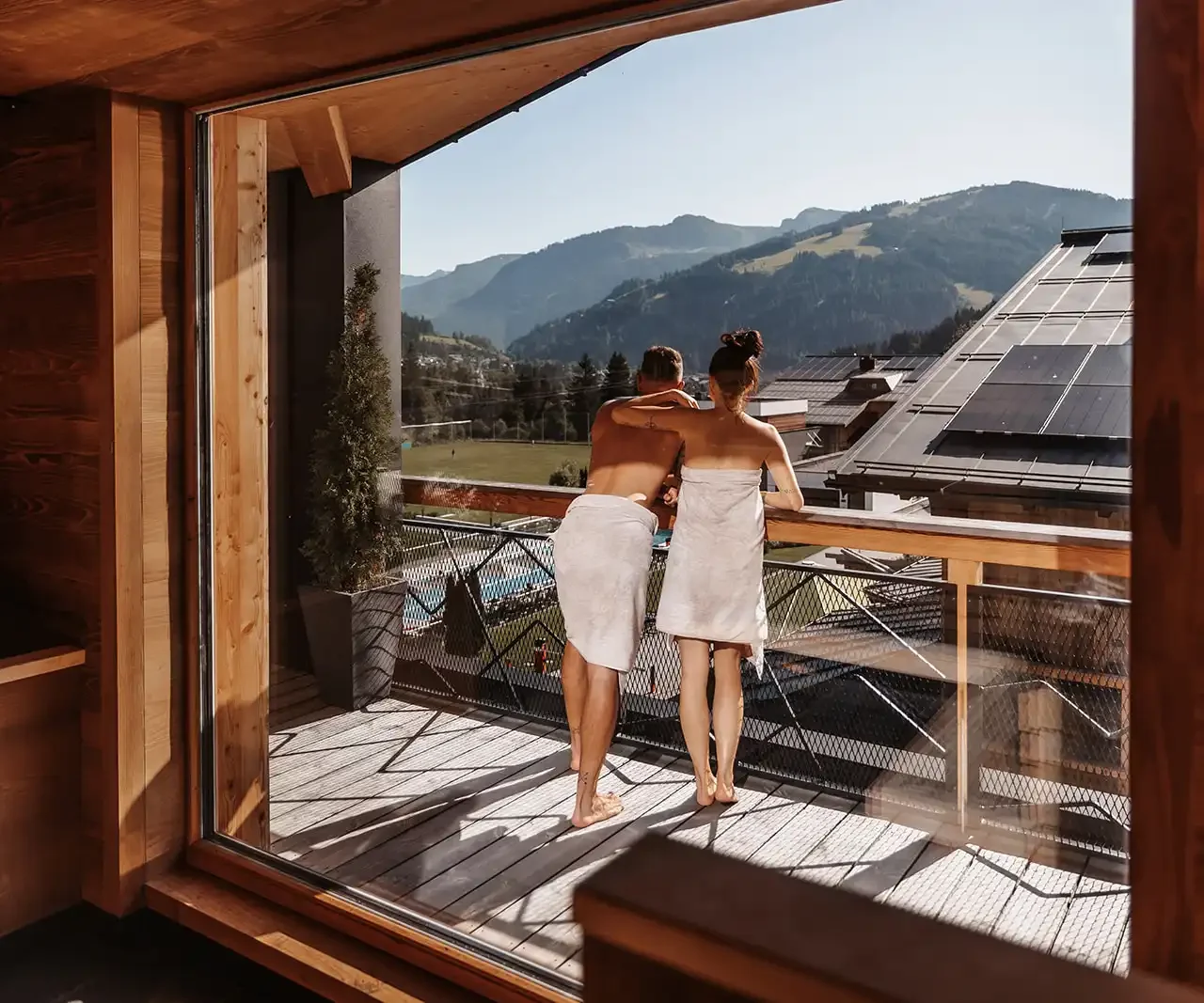Zweisamkeit mit Ausblick – ein Paar genießt im Hofgut Wagrain den Panoramablick auf die Alpen vom Ruhebereich der Skysauna. Warme Holztöne, frische Bergluft und wohltuende Entspannung verschmelzen zu einem besonderen Wohlfühlmoment.
