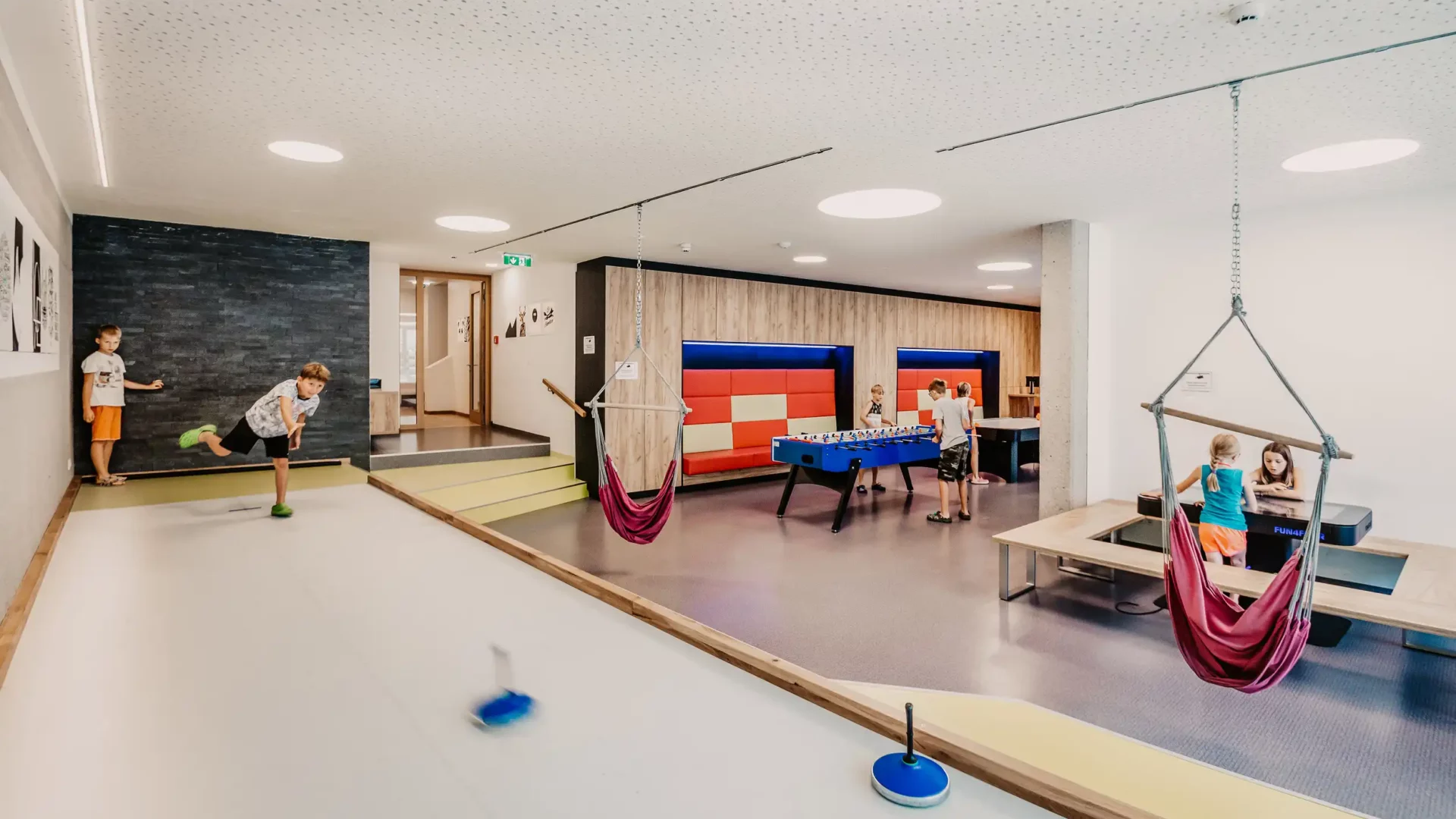 Hofgut-Wagrain-Apartment-Lifestyle-Resort-Erleben-im-Hofgut-für-Kinder-Stockbahn (2) Moderne Indoor-Spielewelt im Hofgut Wagrain mit Kegelbahn, Tischfußball, Hängesesseln und Spieltischen – ideal für Kinder und Familienurlaub in Österreich