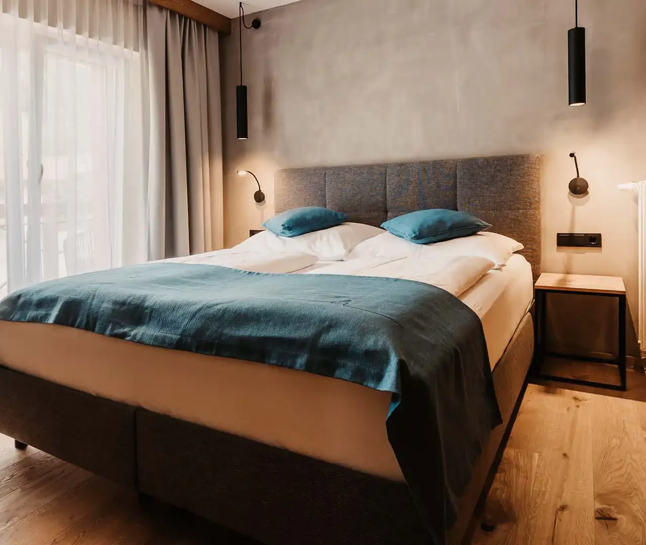 Gemütliches Doppelzimmer mit Boxspringbett, Holzboden und stilvollem Lichtkonzept im alpinen Design