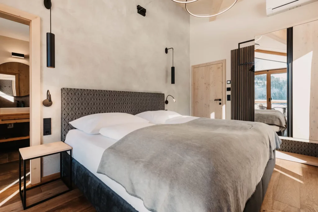 Hofgut-aparment-lifestyle-resort-wagrain-30 Modernes Schlafzimmer im Hofgut Wagrain mit stilvollem Design, gemütlichem Boxspringbett und Balkon mit Bergblick.