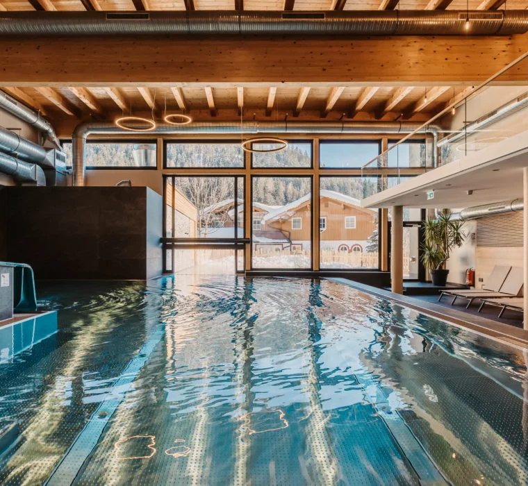 Hofgut-aparment-lifestyle-resort-wagrain Indoor-outdoorpool-128 Stimmungsvolle Aufnahme des Indoor-Pools im Hofgut Wagrain mit Blick ins verschneite Tal – wohltuende Wärme, modernes Design und ein einzigartiger Ort zum Innehalten.