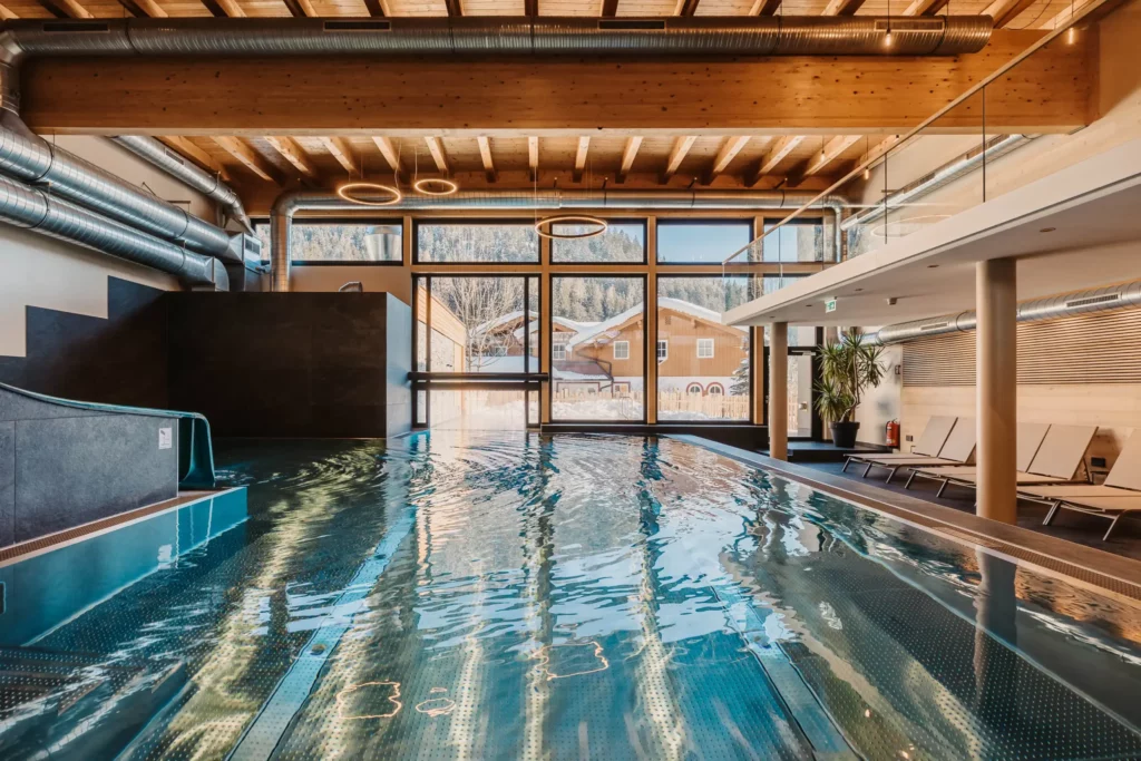 Atmospheric shot of the indoor pool at Hofgut Wagrain with a view of the snow-covered valley - cosy warmth, modern design and a unique place to pause for a moment.