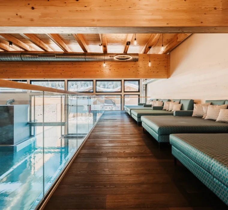 Hofgut-aparment-lifestyle-resort-wagrain-Indoorpool-Wellnessliegen-120 Ruhige Wellnesslounge mit gemütlichen Liegen und Blick auf den Indoorpool im Hofgut Wagrain.