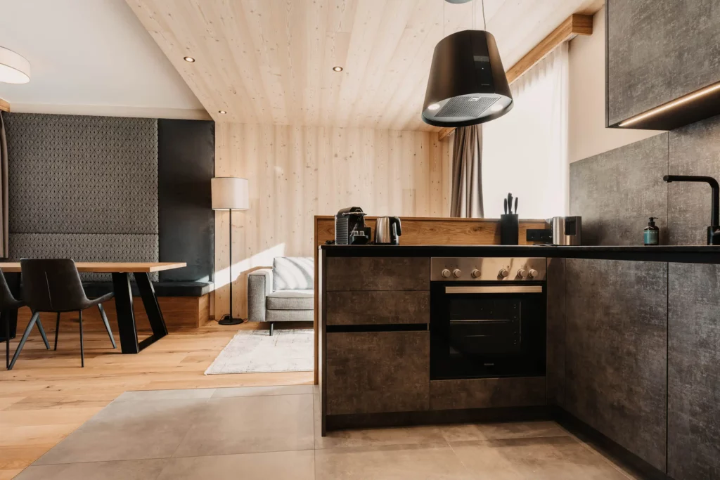 Modern flat kitchen in Hofgut Wagrain with high-quality appliances, dark fronts in concrete look and stylish wooden elements. Open-plan living concept with cosy dining area and alpine design.