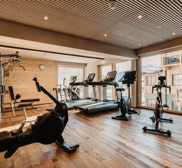 Hofgut-aparment-lifestyle-resort-wagrain-fitnessstudio-115 Modernes Fitnessstudio im Hofgut Wagrain mit hochwertigen Geräten, Holzdesign und Blick auf die verschneiten Berge.
